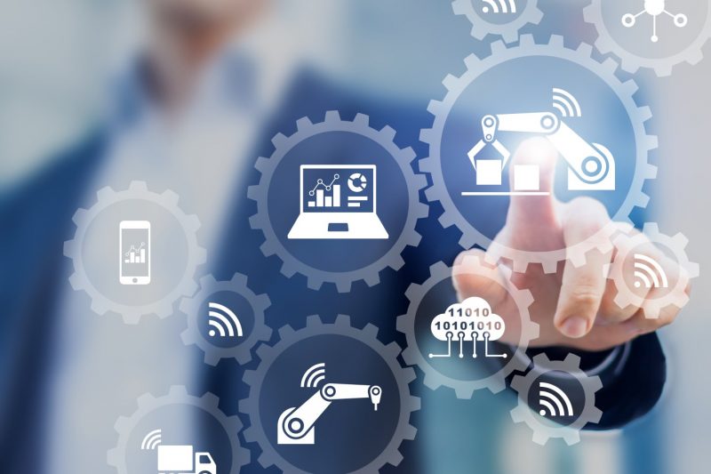 Smart factory and industry 4.0 concept with connected production robots exchanging data with internet of things (IoT) and cloud computing technology, businessman touching interface with icons in gears